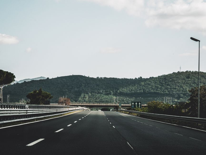 Peaceful highway cutting through lush Italian hills under a clear sky.