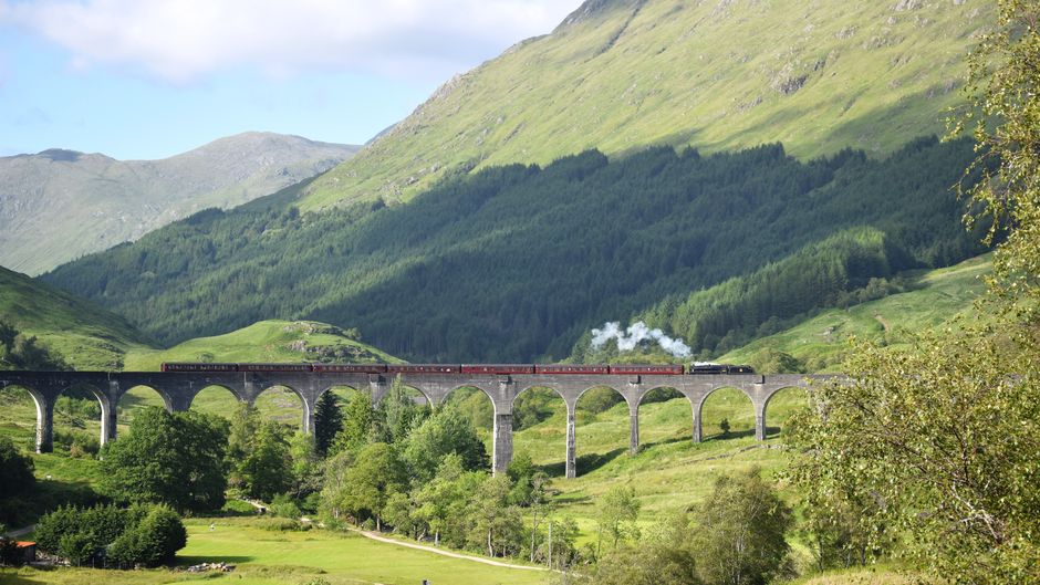Steam train crossing the iconic Glenfinnan Viaduct in Scotland's lush green Highlands.